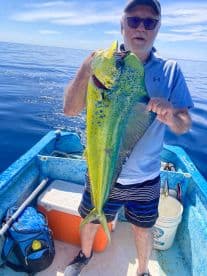 An angler proudly displaying a vibrant Mahi Mahi aboard a small boat in calm ocean waters.