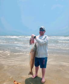 An angler proudly displaying a large Redfish on the beach, showcasing a successful day of fishing along the Texas coast.