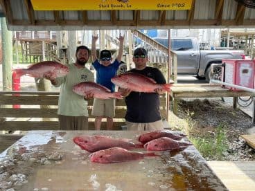A group of anglers proudly displaying their catch of Red Snapper at Shell Beach, Louisiana, with a young boy enthusiastically celebrating.