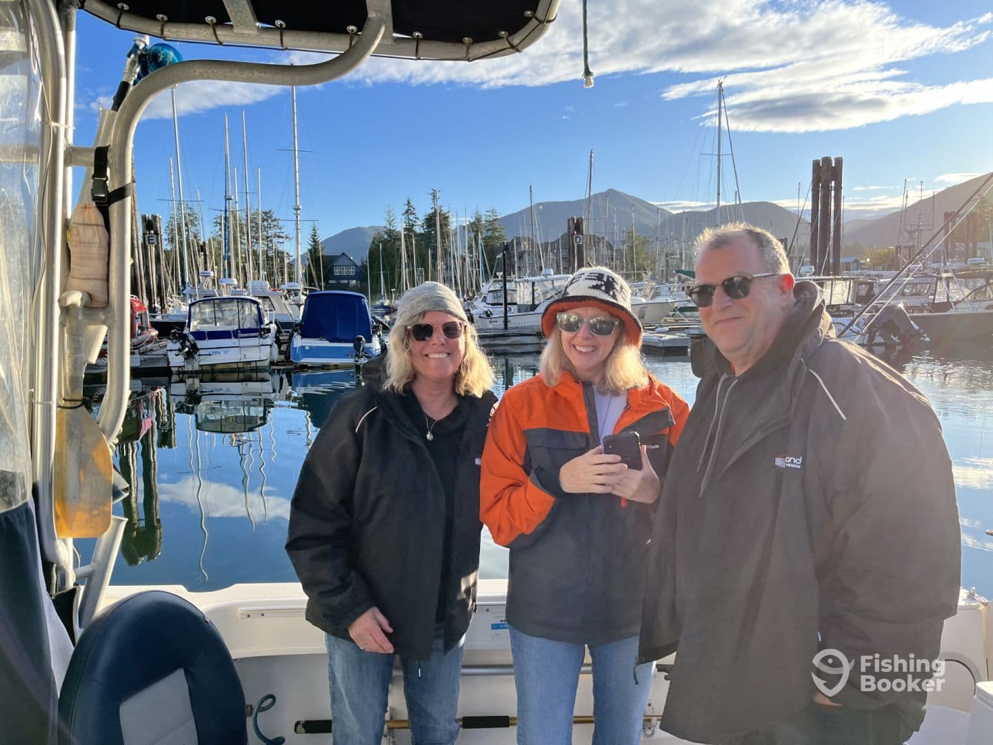 Three friends enjoying a day on the boat at a scenic marina, surrounded by sailboats and mountains.
