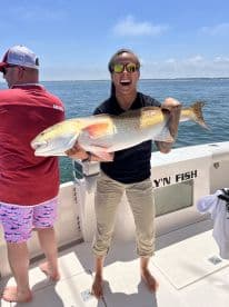 Angler joyfully displaying a large Redfish while fishing on a sunny day, showcasing the excitement of a successful catch.