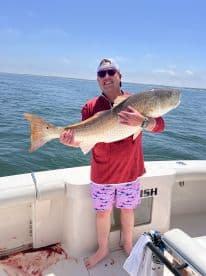 Angler proudly displaying a large Redfish while aboard a fishing boat, enjoying a sunny day on the water.