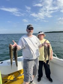 Two anglers proudly displaying their catch of several large fish while aboard a fishing boat, enjoying a day on the water.
