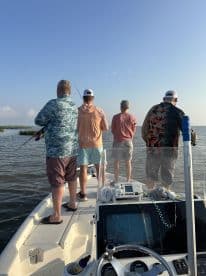 Group of anglers fishing from a boat in a coastal environment, casting lines into the water on a sunny day.