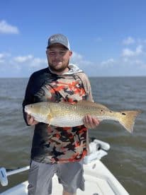 Angler proudly displaying a large Redfish while fishing on a boat in open waters.