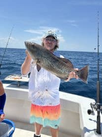 An angler proudly displaying a large Grouper while fishing offshore, showcasing the excitement of a successful catch.