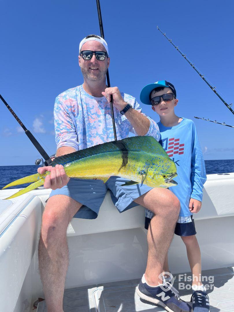 A proud angler and a young boy display a vibrant Mahi Mahi aboard a fishing boat, enjoying a sunny day on the water.