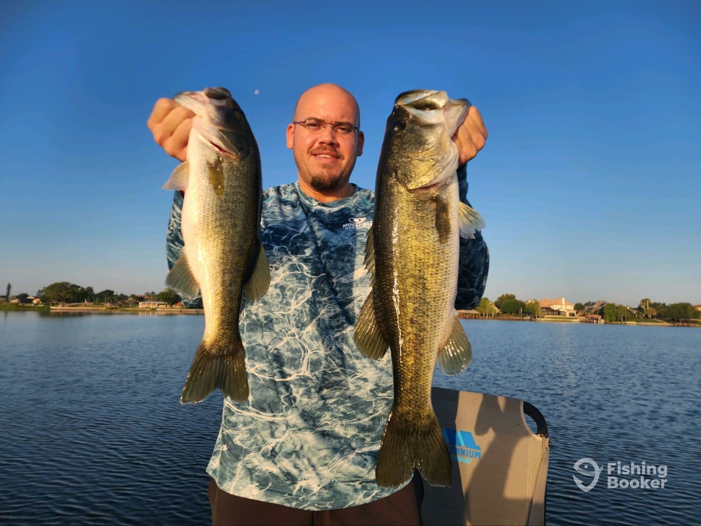 Angler proudly displaying two large Largemouth Bass while fishing on a calm lake, showcasing a successful day on the water.
