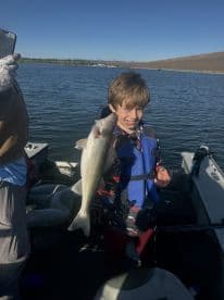 A young angler joyfully displaying a Walleye while fishing on a sunny day in a boat.