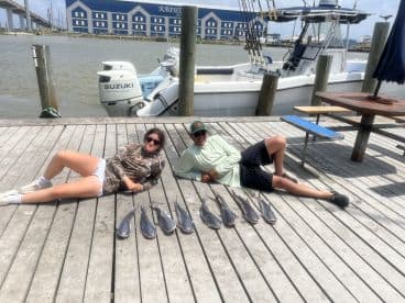 Two anglers relaxing on the dock beside a neat display of several caught fish after a successful fishing trip.