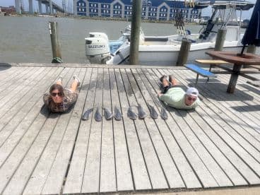 Two anglers lying on the dock next to a display of several caught fish, showcasing their successful fishing trip.