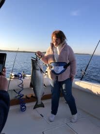 A happy angler proudly displaying a large Salmon on a fishing boat during a serene morning outing.
