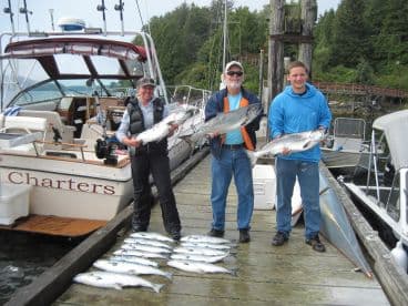 Three anglers proudly displaying their catch of salmon on the dock after a successful fishing trip.