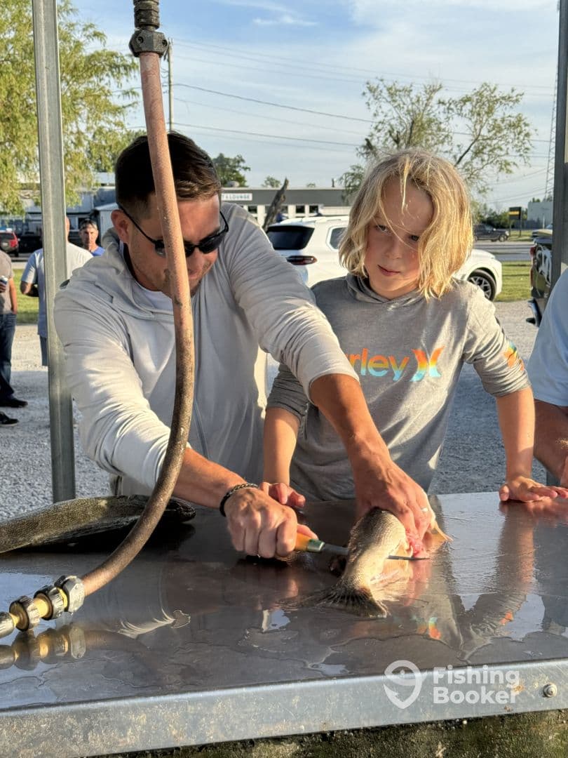 A young boy and an adult are preparing a freshly caught fish at a cleaning station, showcasing a family-friendly fishing experience.