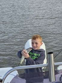 A young angler proudly displaying a caught fish while on a boat, showcasing a fun fishing experience.