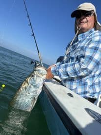 An angler reeling in a large Tarpon while fishing on a sunny day in open waters.