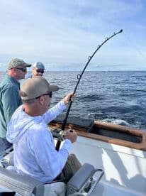 A group of anglers engaged in fishing on a boat, with one angler actively reeling in a catch in open waters.