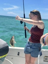 A young angler reeling in a Snapper while fishing on a boat in clear blue waters.