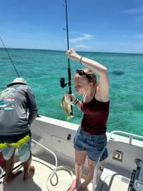 A young angler proudly displaying a freshly caught fish while fishing on a boat in clear turquoise waters.