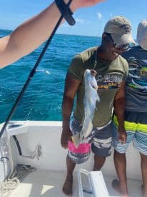An angler joyfully displaying a colorful fish while fishing on a boat in clear blue waters.