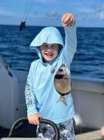 A young angler joyfully holding up a freshly caught fish while fishing on a boat, showcasing a fun day on the water.