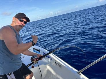An angler actively reeling in a catch while fishing on a boat in deep blue waters, showcasing the excitement of the sport.