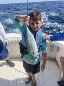 A young angler proudly displaying a fish while aboard a fishing boat, showcasing a fun day on the water.