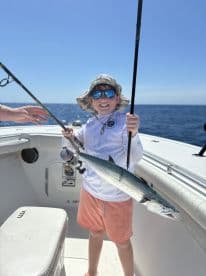 A young angler proudly displaying a caught fish aboard a boat in clear blue waters, showcasing a fun day of fishing.