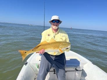 An angler proudly displays a large Redfish while fishing from a small boat in a coastal waterway.