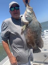 An angler proudly displaying a large Black Drum caught while fishing on a boat in open waters.