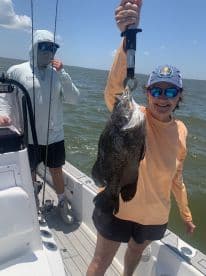 An angler proudly displaying a large Black Drum while fishing on a boat in open waters.