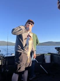Angler proudly displaying a large fish while fishing on a serene lake, surrounded by mountains.