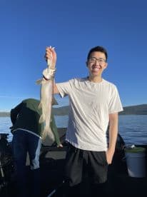 A young angler proudly displaying a large Lake Trout while fishing on a serene lake, with a clear blue sky in the background.
