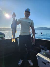 A young angler proudly displaying a large Lake Trout while fishing on a calm lake during sunrise.