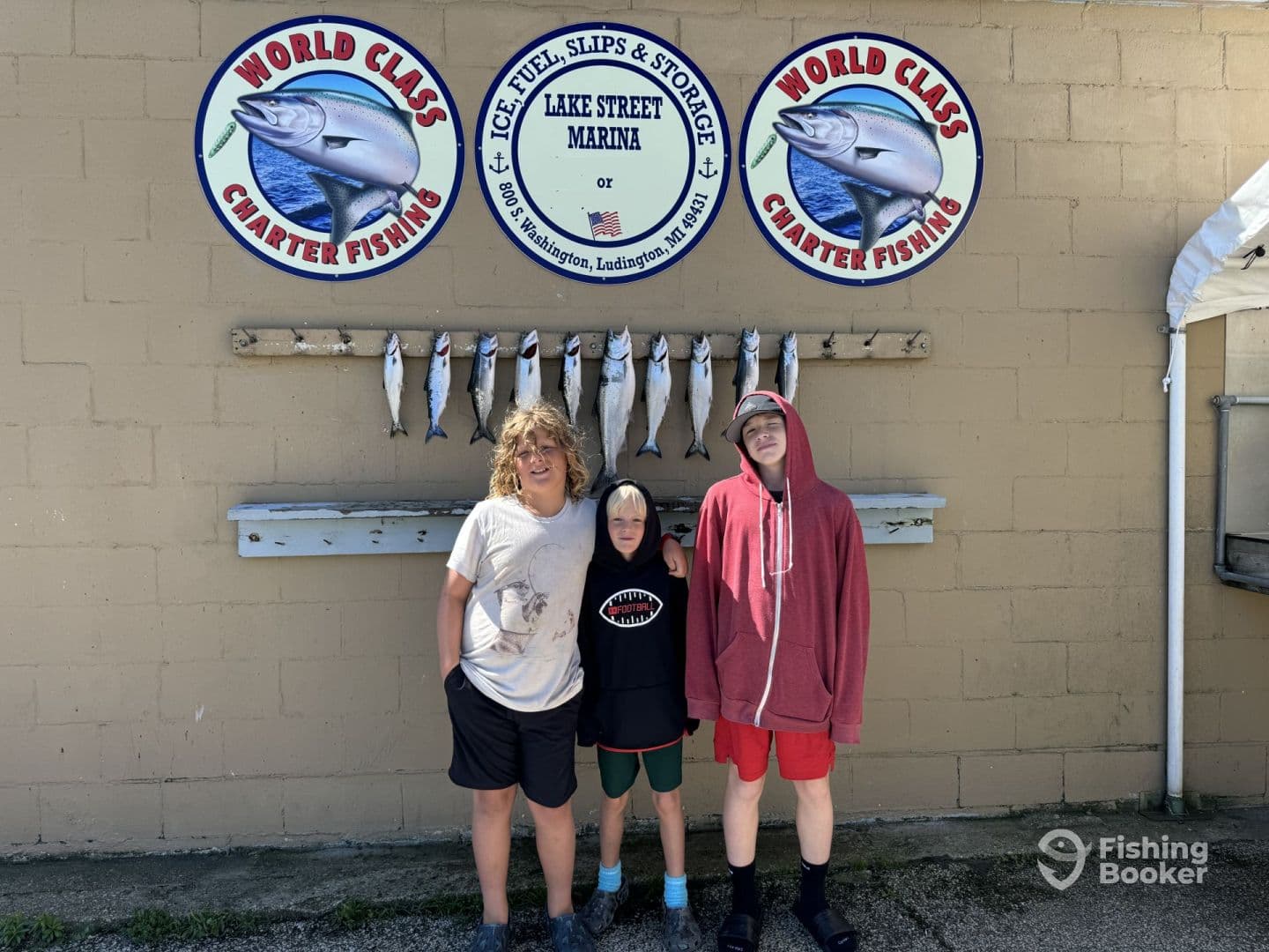 Three young anglers posing in front of a catch board displaying several fish at Lake Street Marina, showcasing their successful fishing trip.