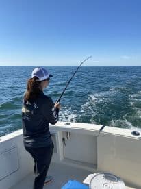 A young angler is actively reeling in a fish while fishing on a boat in open waters, showcasing the excitement of the sport.