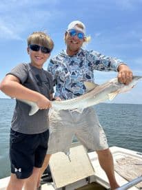 A young angler and an adult proudly displaying a caught shark while fishing on a sunny day.