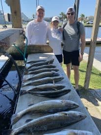 A group of anglers proudly posing with a catch of Speckled Trout displayed on a cleaning table after a successful fishing trip.