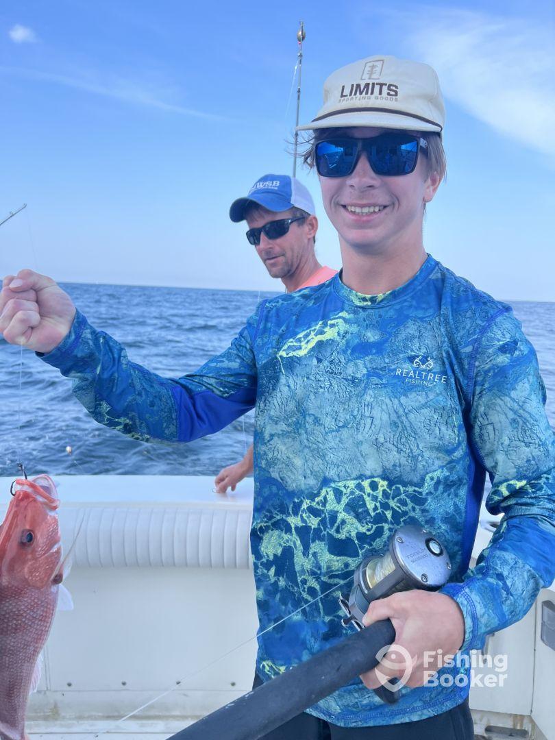 A young angler proudly displaying a Red Snapper while fishing offshore, with a fellow angler in the background.