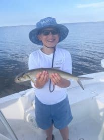 A young angler proudly displaying a caught fish while on a boat, enjoying a sunny day on the water.