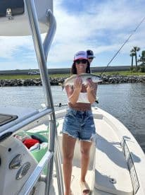 An angler proudly displaying a Speckled Trout while aboard a fishing boat, enjoying a sunny day on the water.