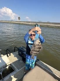 A young angler proudly displaying a large Black Drum caught while fishing from a small boat in a coastal waterway.