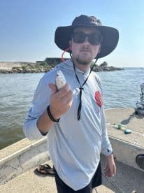 Angler holding a small fish while fishing from a boat, showcasing a sunny day on the water.