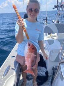 An angler proudly displaying a large Red Snapper while fishing on a boat in open waters.