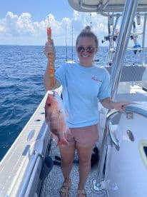 Angler proudly displaying a large Red Snapper while fishing on a boat in open water.