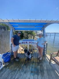 Two anglers posing with a display of freshly caught fish on a board at a waterfront location, showcasing their successful fishing trip.