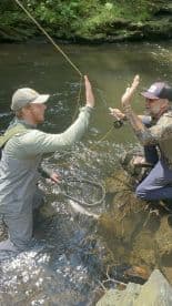 Two anglers celebrating a successful catch while fly fishing in a scenic river setting.
