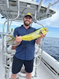 Angler proudly displaying a vibrant Mahi Mahi aboard a fishing boat in open waters.