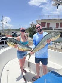 Two anglers proudly displaying their catch of Mahi Mahi on a sunny day aboard a fishing boat.