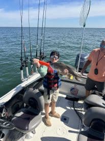 A young angler proudly displaying a Redfish while fishing on a charter boat, showcasing the excitement of a successful catch.